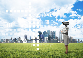 Camera headed woman standing on green grass against modern cityscape