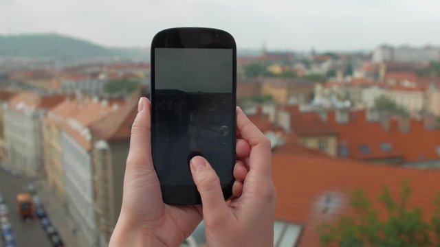 female hands holding smartphone and taking photos of panorama of Prague