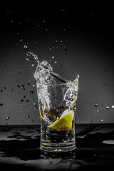 Half Lemon dropped in a glass of water with water splashes with a black to grey background