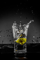 Half Lemon dropped in a glass of water with water splashes with a black to grey background