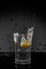 Half Lemon dropped in a glass of water with water splashes with a black to grey background