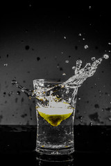 Half Lemon dropped in a glass of water with water splashes with a black to grey background