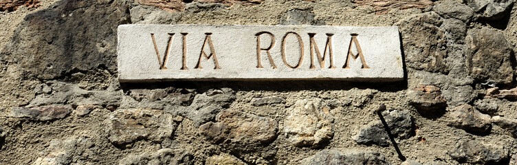 Marble street sign VIA ROMA in an ancient village in Italy. On the background a stone wall.