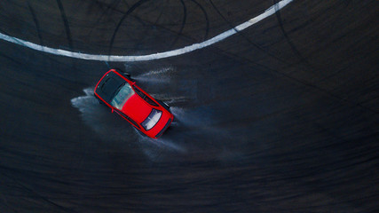 Aerial top view professional driver drifting red car on wet asphalt race track with water splash,...