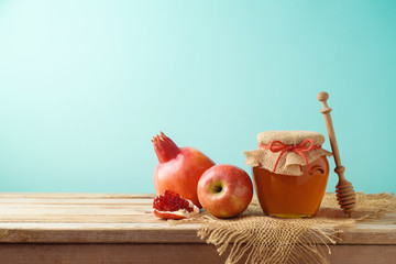 Jewish holiday Rosh Hashanah background with honey jar, apple and pomegranate on wooden table.