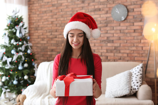 Beautiful young woman in Santa hat with gift box at home. Celebrating Christmas