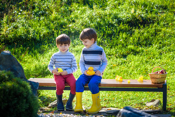 Little kids brothers Sitting on wooden bench play with rubber ducks.