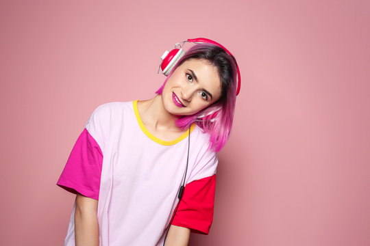 Young woman with trendy hairstyle listening to music against color background