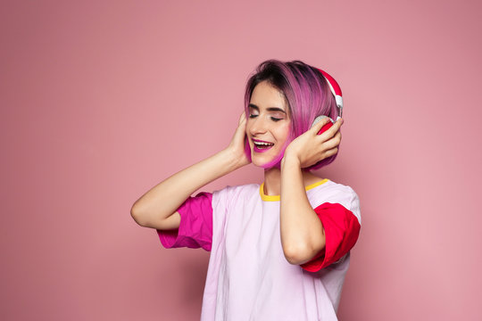 Young woman with trendy hairstyle listening to music against color background