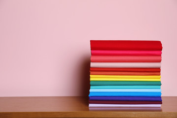 Pile of bright t-shirts on table against color background