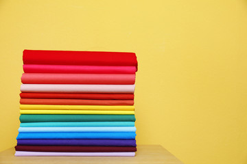 Pile of bright t-shirts on table against color background