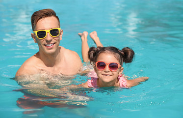 Young man teaching his daughter to swim in pool