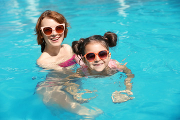 Young woman teaching her daughter to swim in pool