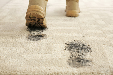 Person in dirty shoes leaving muddy footprints on carpet
