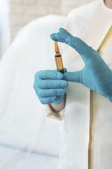 A gloved hand holding an ampoule with medicine on the background of the couch.