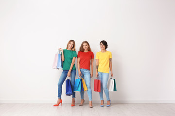 Naklejka premium Group of young women with shopping bags near light wall