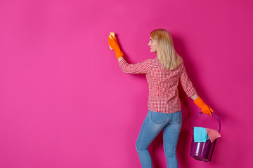 Woman in gloves cleaning color wall with rag