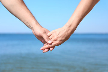 Happy couple holding hands at beach on sunny day, closeup