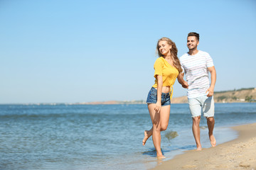Fototapeta na wymiar Happy young couple walking at beach on sunny day