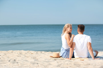 Fototapeta premium Happy young couple sitting together at beach on sunny day
