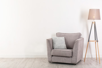 Comfortable armchair and lamp near wall with space for design. Stylish interior elements