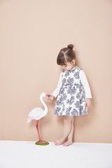 Adorable baby girl in a festive dress playing with a wild duck in a beautiful sunny autumn park