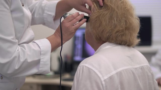 Nurse examines the ear of an adult woman.