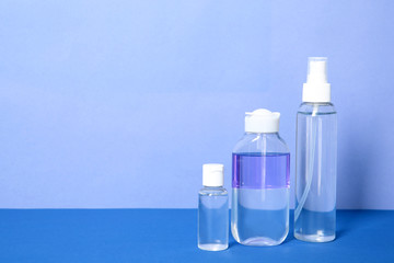 Different cosmetic bottles on table against color background