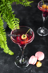 cosmopolitan or margarita cocktail garnished with a macaroons and berries on a dark background with a green flower