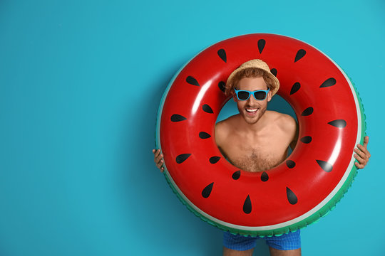 Happy young man with inflatable ring on color background