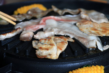 meat, bacon and streaky pork grilled on the black electric grill with corn boil at the side of it.