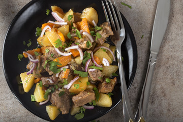 Baked potatoes, pork meat and carrots on plate with herbs
