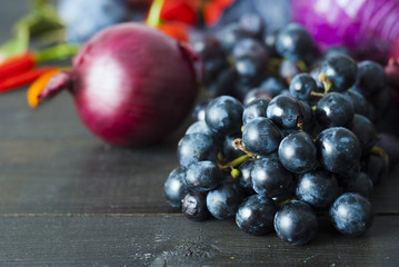 chili peppers, egg plant, grapes, plums on black wood table background