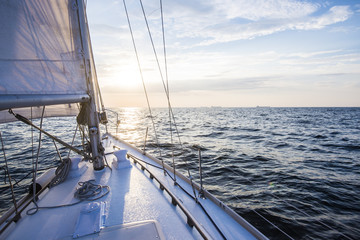 Fototapeta premium Żeglarstwo o zachodzie słońca. Widok z pokładu jachtu na dziób i żagle. Morze Bałtyckie, Łotwa