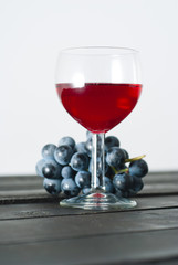 glass of red wine and grapes on black wood table background
