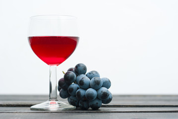 glass of red wine and grapes on black wood table background