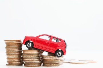 Little red car over a lot of money stacked coins with isolated white background . for loans costs...