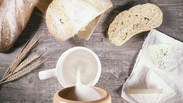 Slow motion from a clay jug of milk pour into a mug near the sliced bread and cheese with mold top view