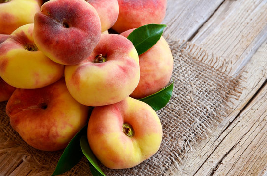 Chinese flat donut peaches with leaves on on old wooden table also known as  Saturn donut, Doughnut peach,
Paraguayo.Healthy eating or diet concept.Selective focus.