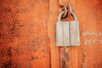 Padlock on a rusty brown metal door. Processed for vintage tone effect. Rusted iron orange plate door with handle and lock