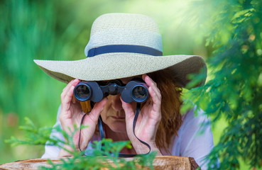 hidden between bushes, a woman secretly observes with binoculars