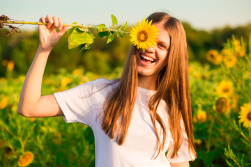 Happy joyful girl with sunflower enjoying nature and laughing on summer sunflower field 