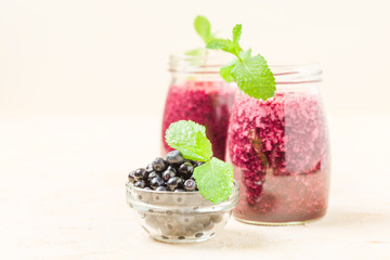 Blueberry smoothie decorated with fresh green mint leaves and raw ripe berries on yellow pastel background.