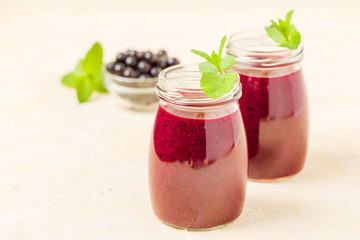 Currant smoothie decorated with fresh green mint leaves and raw ripe berries on yellow pastel background.