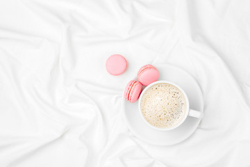 Cup of coffee and macaroons on bed. Flat lay, top view