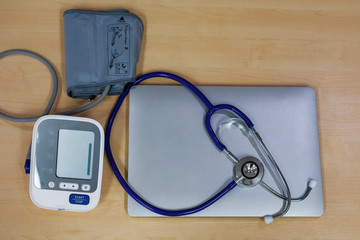 Stethoscope, measuring blood pressure and laptop on wooden desk for analysis of medical results.