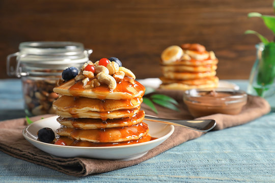 Stack of tasty pancakes with berries, nuts and syrup on table