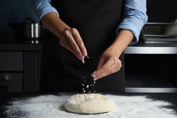 Woman sprinkling dough for pastry with flour on table