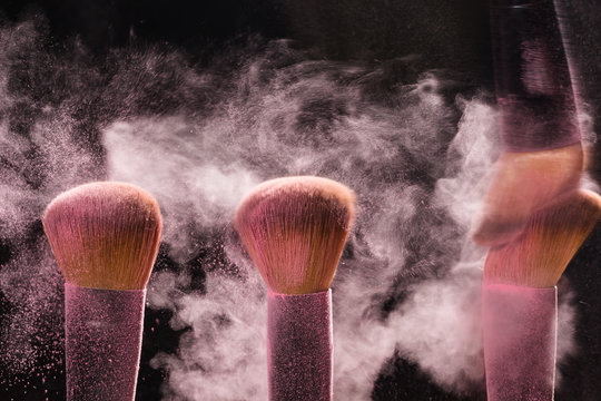 Three brushes for makeup with pink make-up mineral powder in motion on a black background