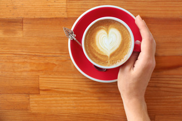 Woman with cup of fresh aromatic coffee at wooden table, top view